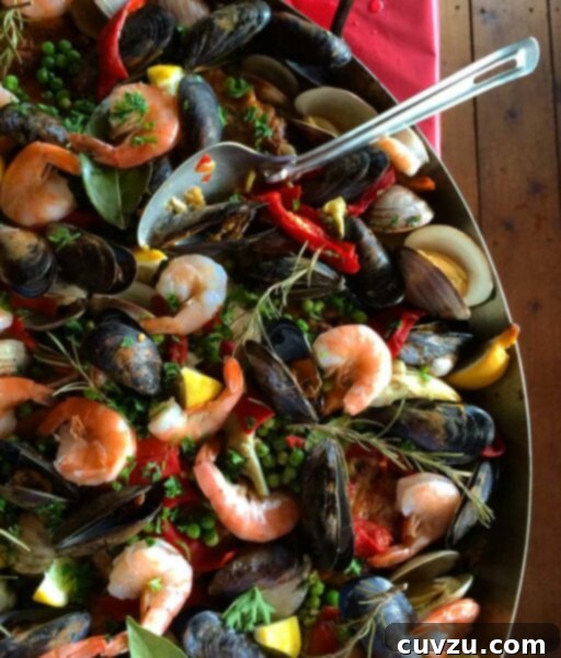A large Dutch oven brimming with colorful paella, featuring shrimp, mussels, red peppers, peas, lemon slices, and parsley, ready to be served.