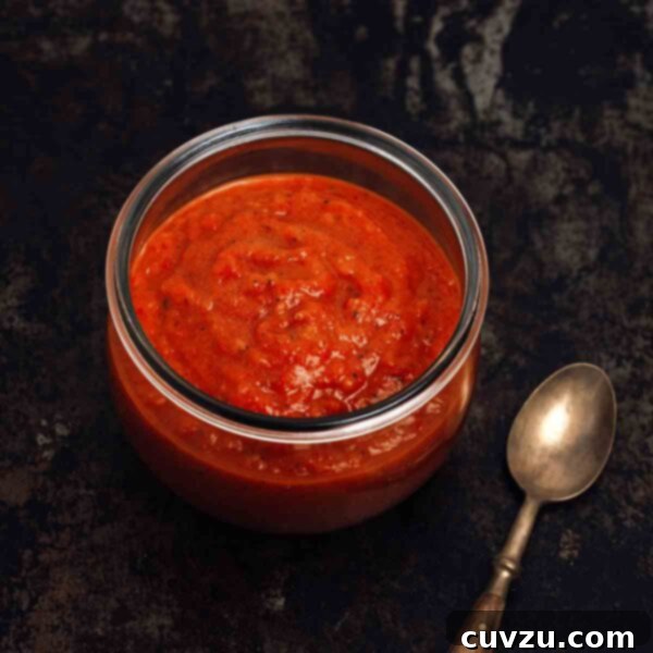 A jar of red homemade sriracha hot sauce on a black background, with a small spoon beside it, ready for tasting.
