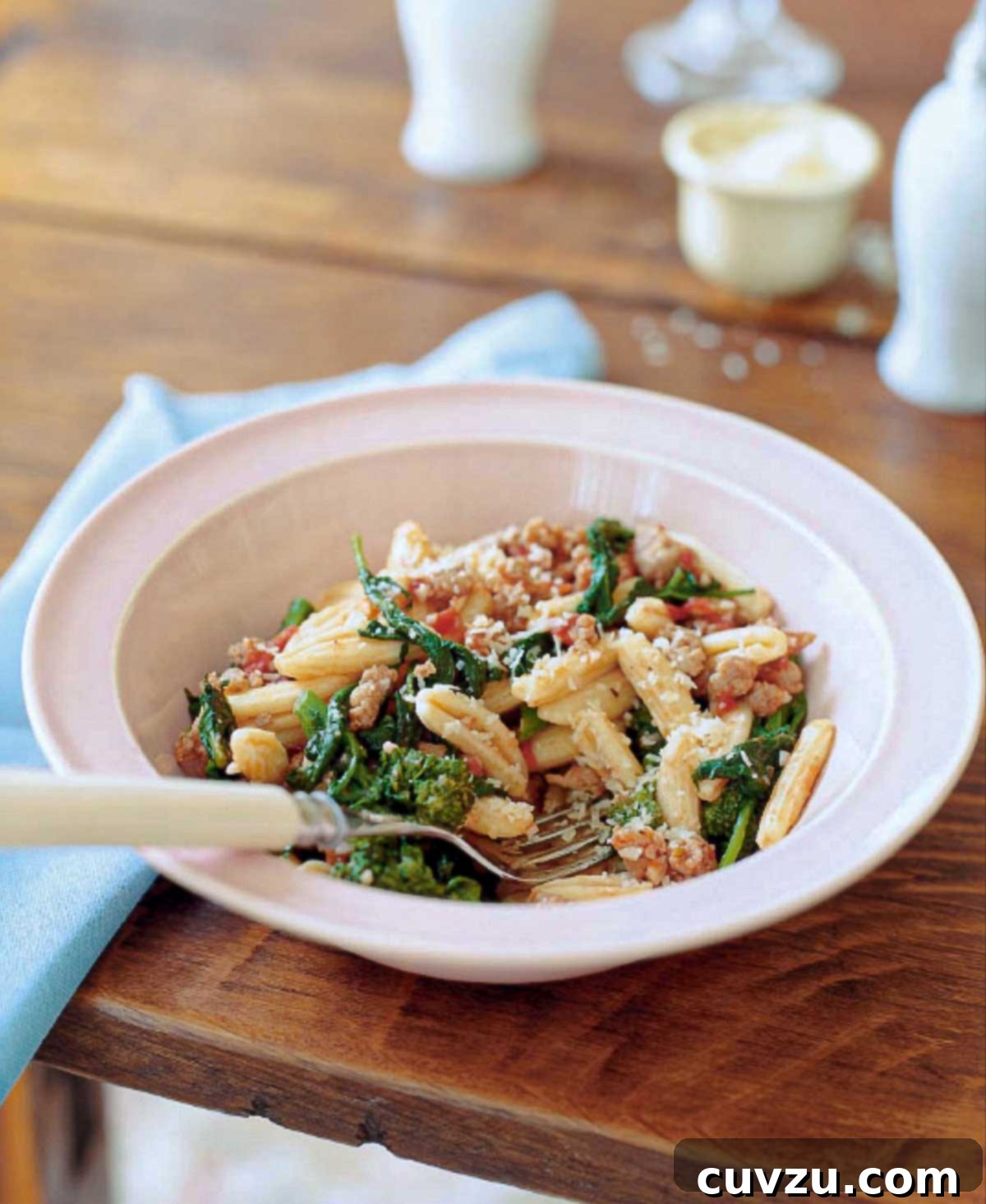 Bowl of cavatelli with turkey sausage, tomato, and broccoli rabe on a table, with a spoon.