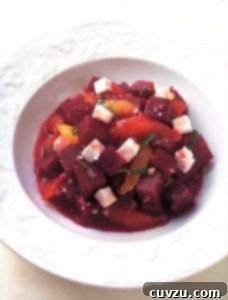 A white bowl filled with a beet salad with feta and orange and sliced mint leaves, photographed from an appealing angle.