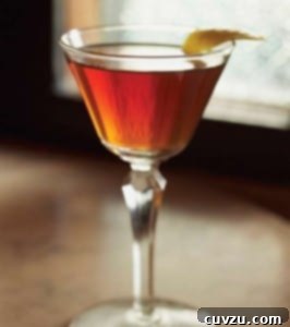A classic Manhattan cocktail in a coupe glass with a lemon garnish.