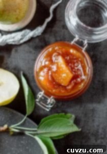 An open jar of pear chutney with a cut pear and some leaves lying beside it.