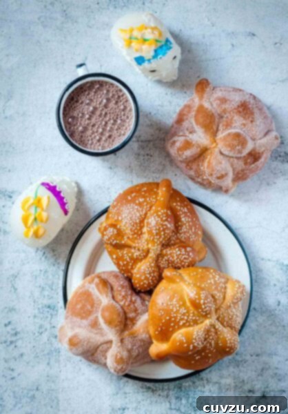Day of the Dead bread on a plate, two with sugar and two with white sesame seeds, beside a cup of Mexican hot chocolate and two sugar skulls.