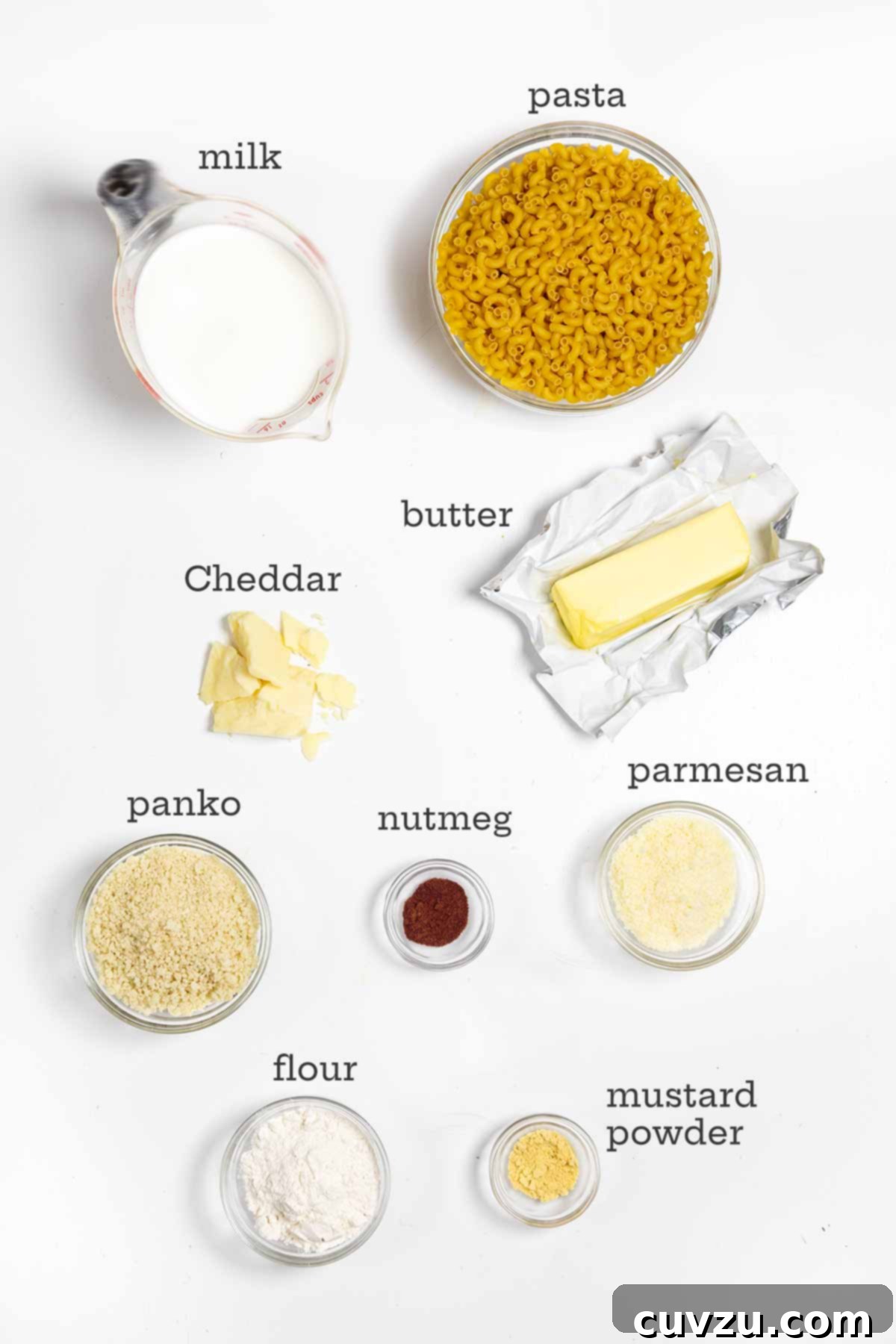 Ingredients for baked macaroni and cheese, including pasta, Cheddar cheese, panko, nutmeg, and butter.