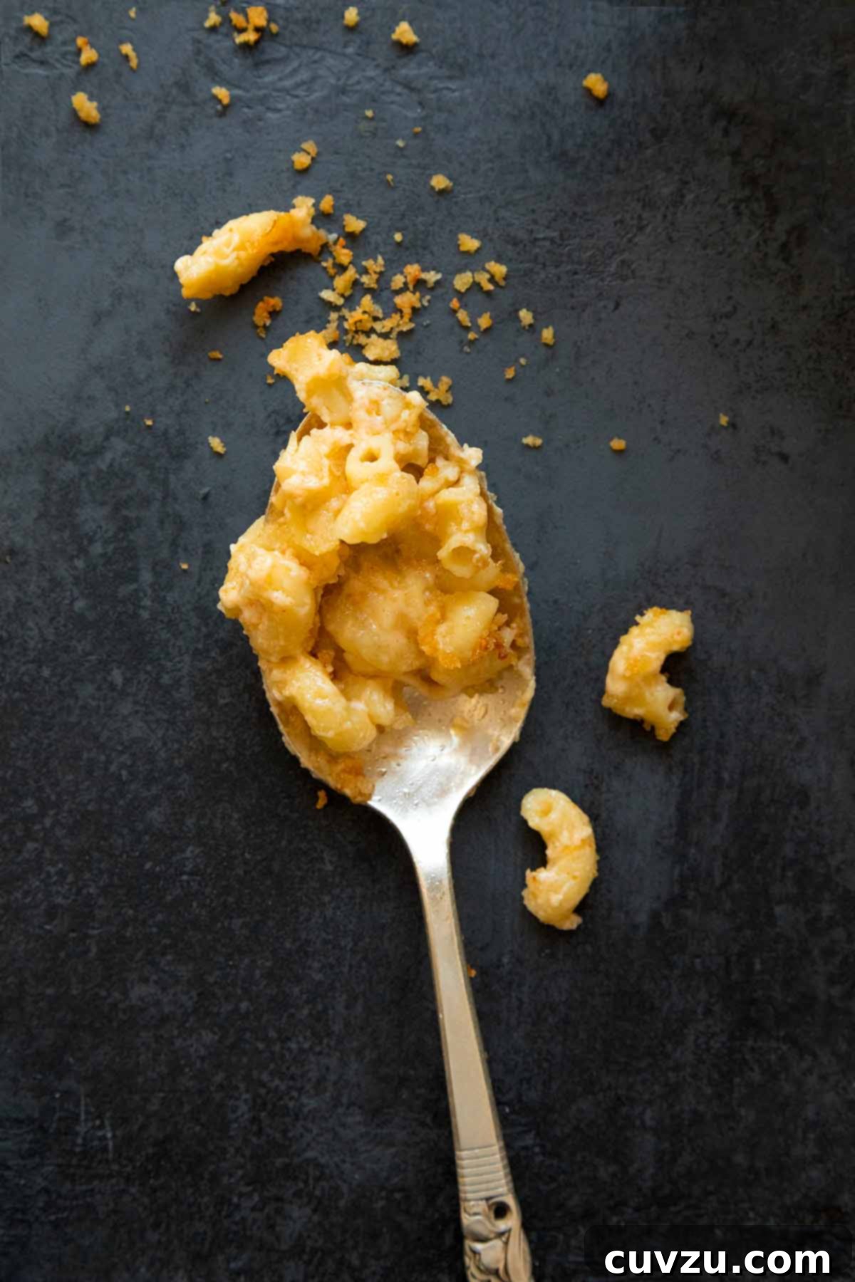 A spoon full of baked macaroni and cheese on a black background.