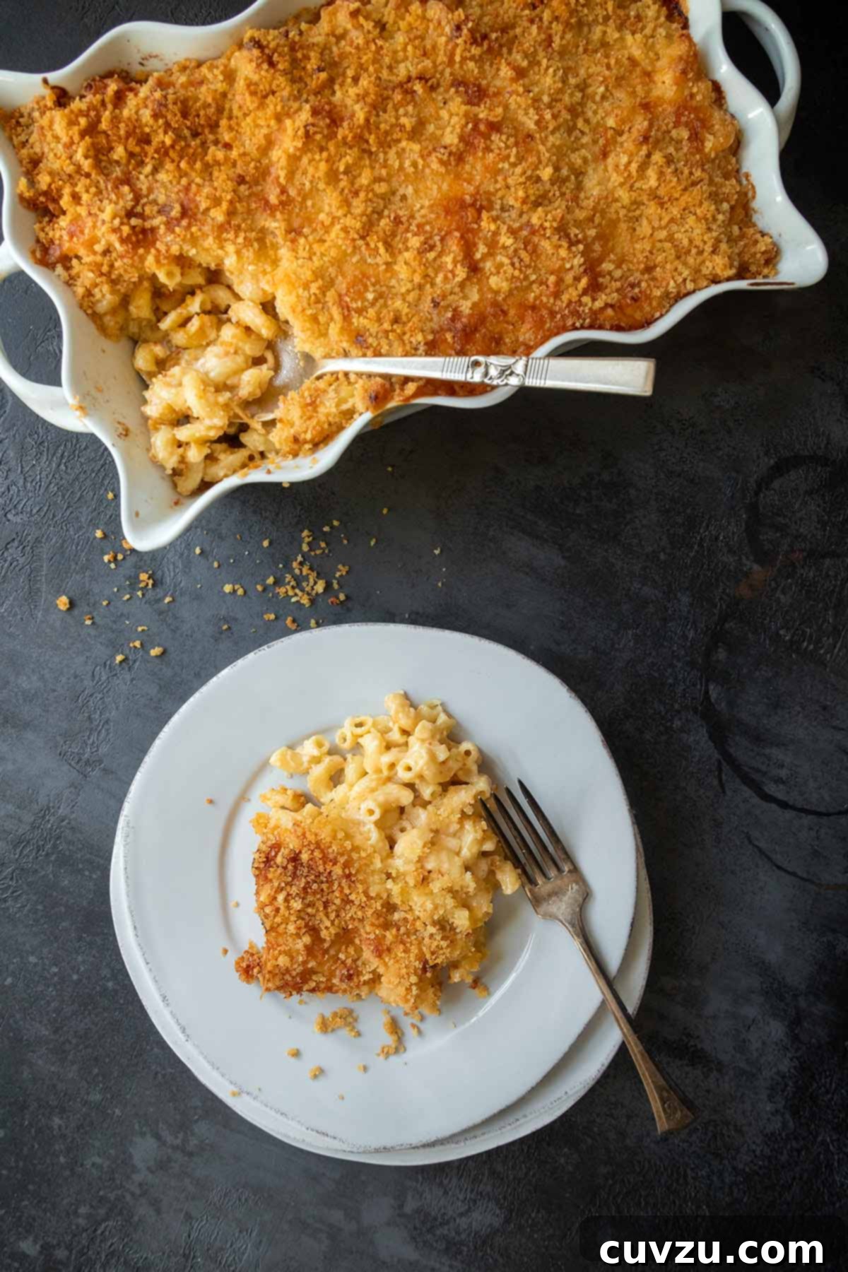 A casserole dish of mac and cheese with a plate with a portion of the pasta.