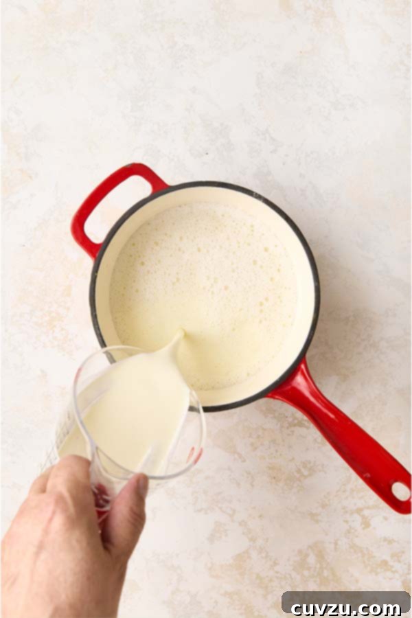 Authentic Italian Creamy Pistachio Gelato 8 Pouring heavy cream from a glass measuring cup into a red pot containing the warm gelato base.