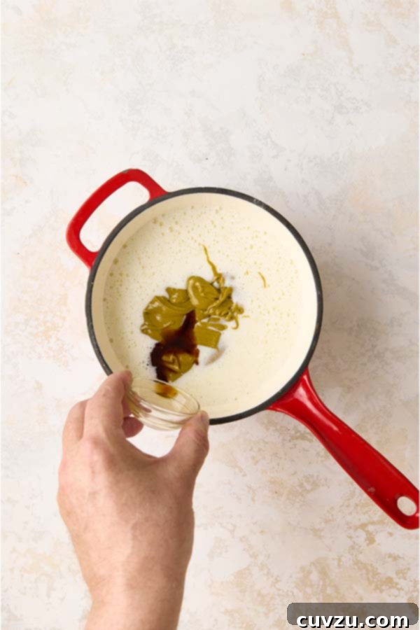 Authentic Italian Creamy Pistachio Gelato 9 Adding rich pistachio paste and aromatic vanilla extract to the warm milk and cream mixture in a red pot.