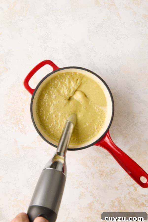 Authentic Italian Creamy Pistachio Gelato 10 An immersion blender vigorously mixing the pistachio gelato base until completely smooth in a red pot.