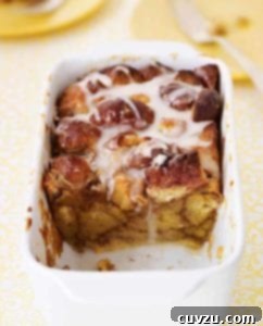 White casserole dish half filled with chunks of doughnuts in a pudding drizzled with a sugar glaze