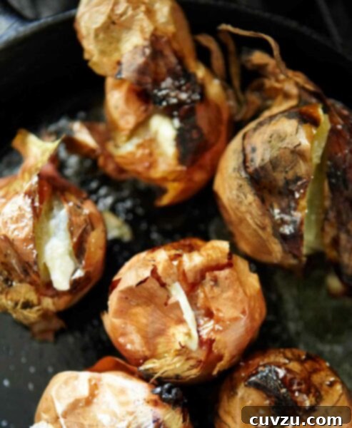 A cast-iron skillet with 8 whole roasted onions with papery skins and creamy interiors.