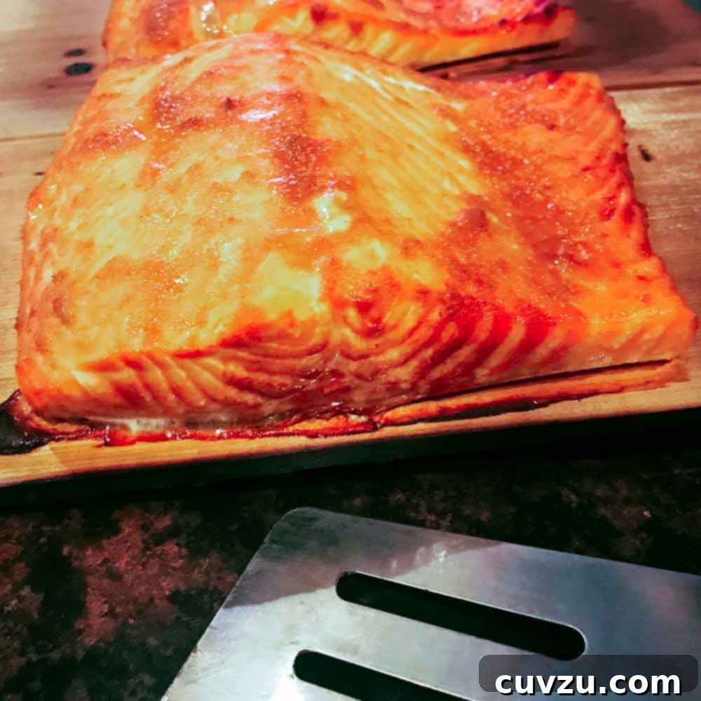 Two golden fillets of cedar plank–grilled salmon presented on a wooden board, glistening with glaze.