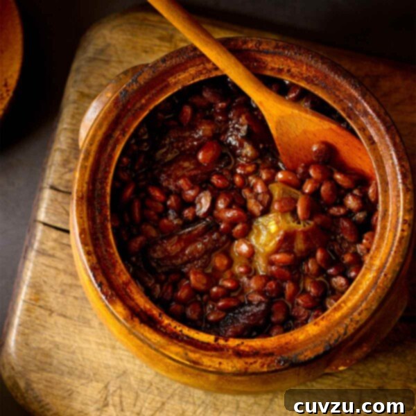 A pot of Appalachian cider baked beans with a wooden spoon placed on a wooden chair, showcasing the rich color and inviting texture of the dish.