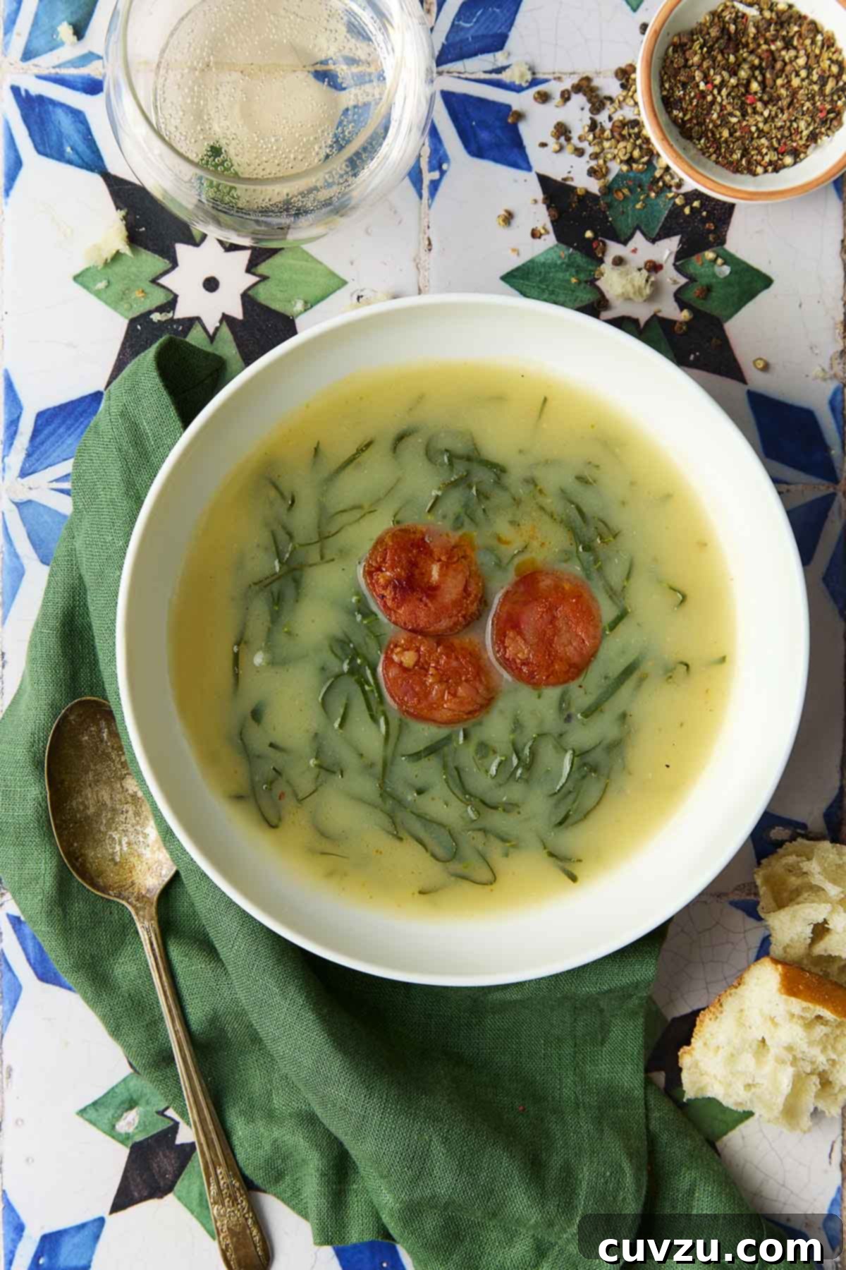 Caldo Verde: Portugal's Iconic Green Soup 2 A white bowl of Caldo Verde, or Portuguese kale soup (green broth) with thinly sliced kale and three chouriço coins floating in the center, garnished with a drizzle of olive oil.