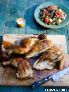 A wooden cutting board with a carved grilled Greek chicken and a knife resting beside it, ready to be served.