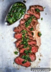 A sliced steak chimichurri with a gravy boat filled with chimichurri on the side.