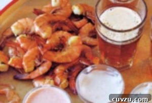 Shrimp with three dipping sauces piled on a platter, beside a glass of ale