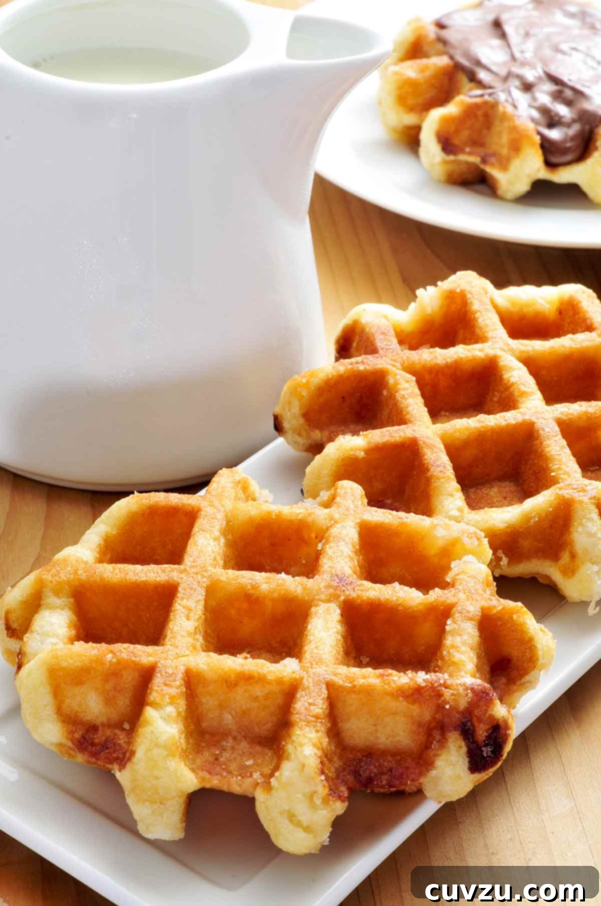 Liege Waffles: Belgian Bliss 2 Two authentic Belgian Liège waffles on plates, with a pitcher of cream in the background, inviting a taste of traditional Belgian street food.