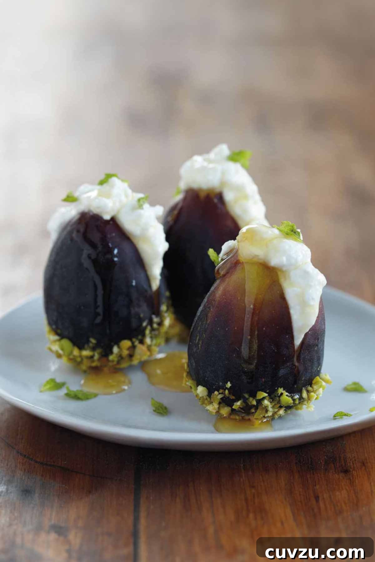 Honeyed Figs with Creamy Ricotta 2 Three ripe figs, halved and generously filled with creamy ricotta cheese, beautifully arranged on a white plate. Each fig is garnished with a glistening drizzle of honey, chopped green pistachios, and delicate mint leaves, showcasing a simple yet sophisticated dessert.