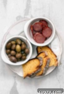 Slices of broa, or Portuguese corn bread, on a plate with a bowl of olives and a bowl of sliced chouriço.