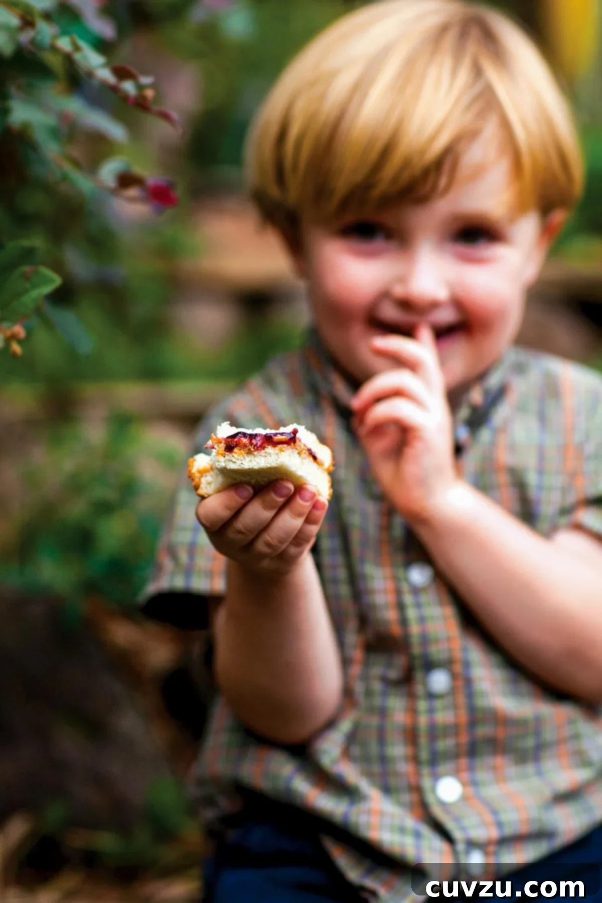 Homemade Concord Grape Jam 2 A small boy holding a partially eaten peanut butter and homemade Concord grape jam sandwich, smiling joyfully.