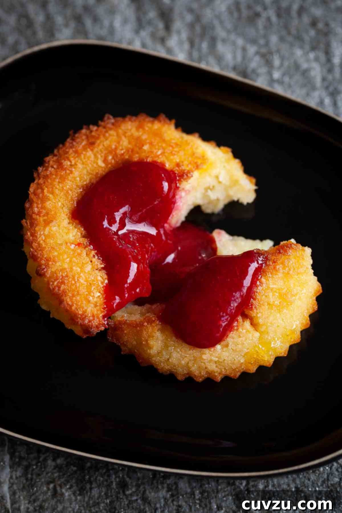 Golden Portuguese Coconut Delights 3 A perfectly halved Portuguese coconut custard tart, revealing its creamy custard filling and a golden toasted coconut topping, served on a sleek black plate.