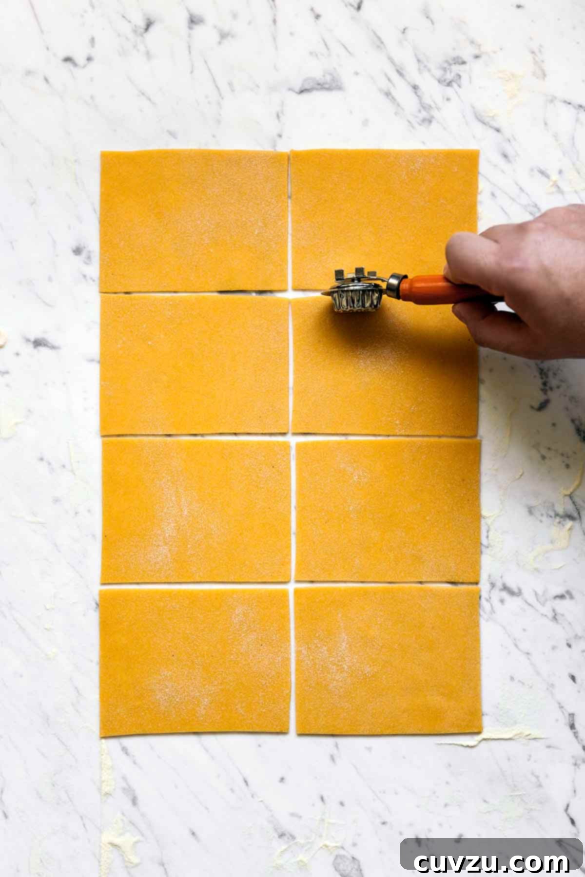 Golden Pumpkin Pasta Dough 4 A person cutting a large sheet of pumpkin pasta dough into neat rectangles on a floured surface.