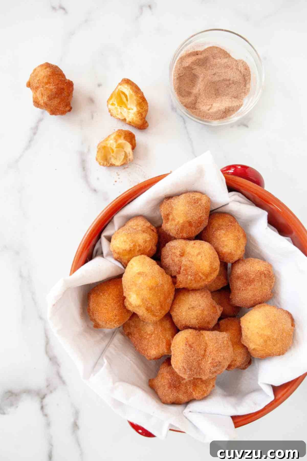 Sonhos: Portugal's Dreamy Doughnuts 4 An overhead view of a red bowl brimming with Sonhos, each golden orb generously coated with cinnamon sugar, highlighting their inviting texture.