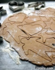 A sheet of raw black pepper cookie dough with shapes--men, stars reindeer, hearts--cut into it