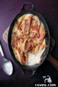 A cast-iron baking dish filled with fennel baked in cream on a wooden board.