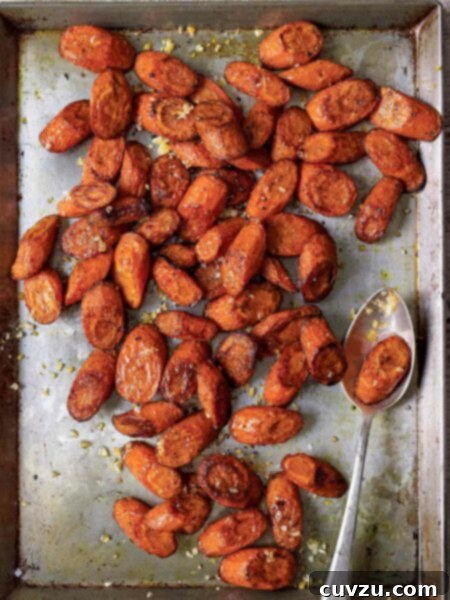 Allspice-Kissed Roasted Carrots 5 A large metal sheet pan filled with slices of roasted carrots with allspice, sea salt and preserved lemons, with a serving spoon.