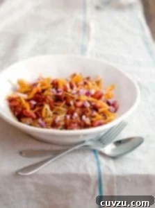 A white bowl of turkey Cincinnati chili with a fork and spoon resting beside it.