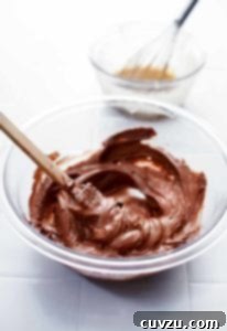 A glass mixing bowl filled with homemade nutella and a spatula rests inside the bowl