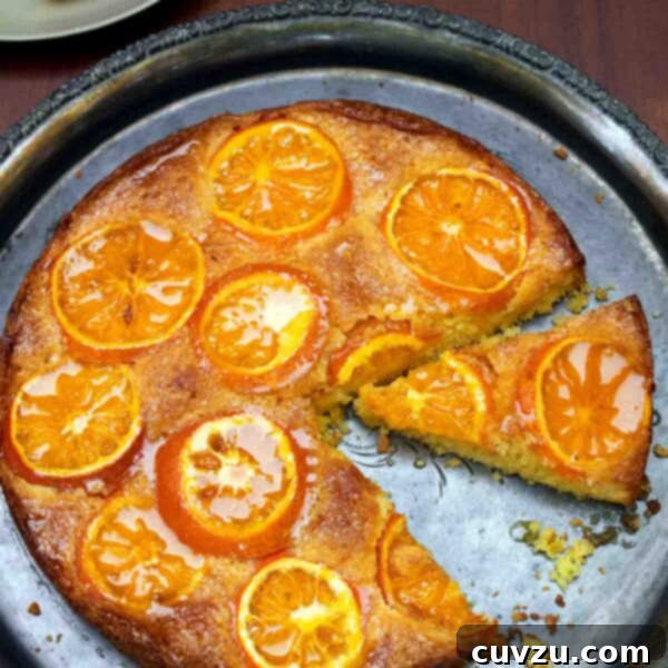 A clementine cake on a round silver platter with one slice on a plate beside it.