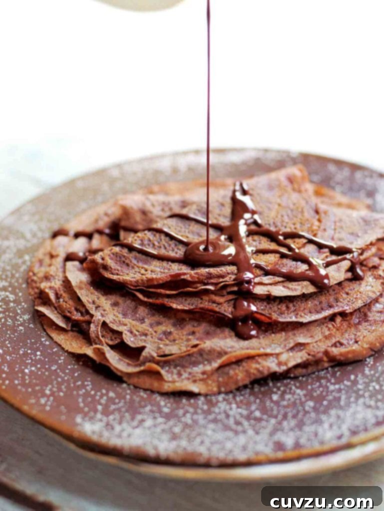 Effortless Chocolate Crepes 2 A beautifully stacked tower of Tom Aikens' chocolate crêpes, generously drizzled with a rich chocolate sauce, enticingly ready to be served.