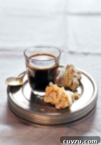 Two pieces of almond biscotti on a stack of plates with a glass of coffee
