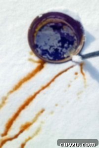A bucket of maple syrup in the snow with streaks of maple syrup snow nearby, perfect for making maple syrup snow candy.