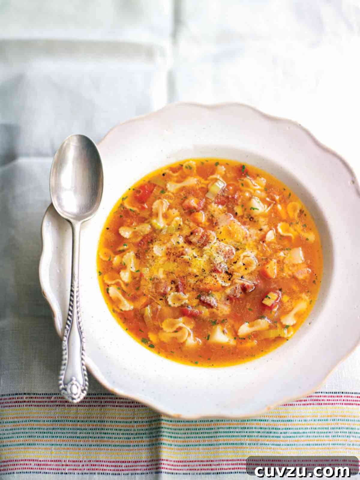 Hearty Pancetta Potato Pasta Soup 2 A rustic white bowl overflowing with steaming pasta soup, featuring visible chunks of potato, tender pasta, and savory pancetta, artfully placed on a soft linen cloth with a spoon resting invitingly on its edge. This image perfectly captures the warmth and richness of a classic Italian comfort food.