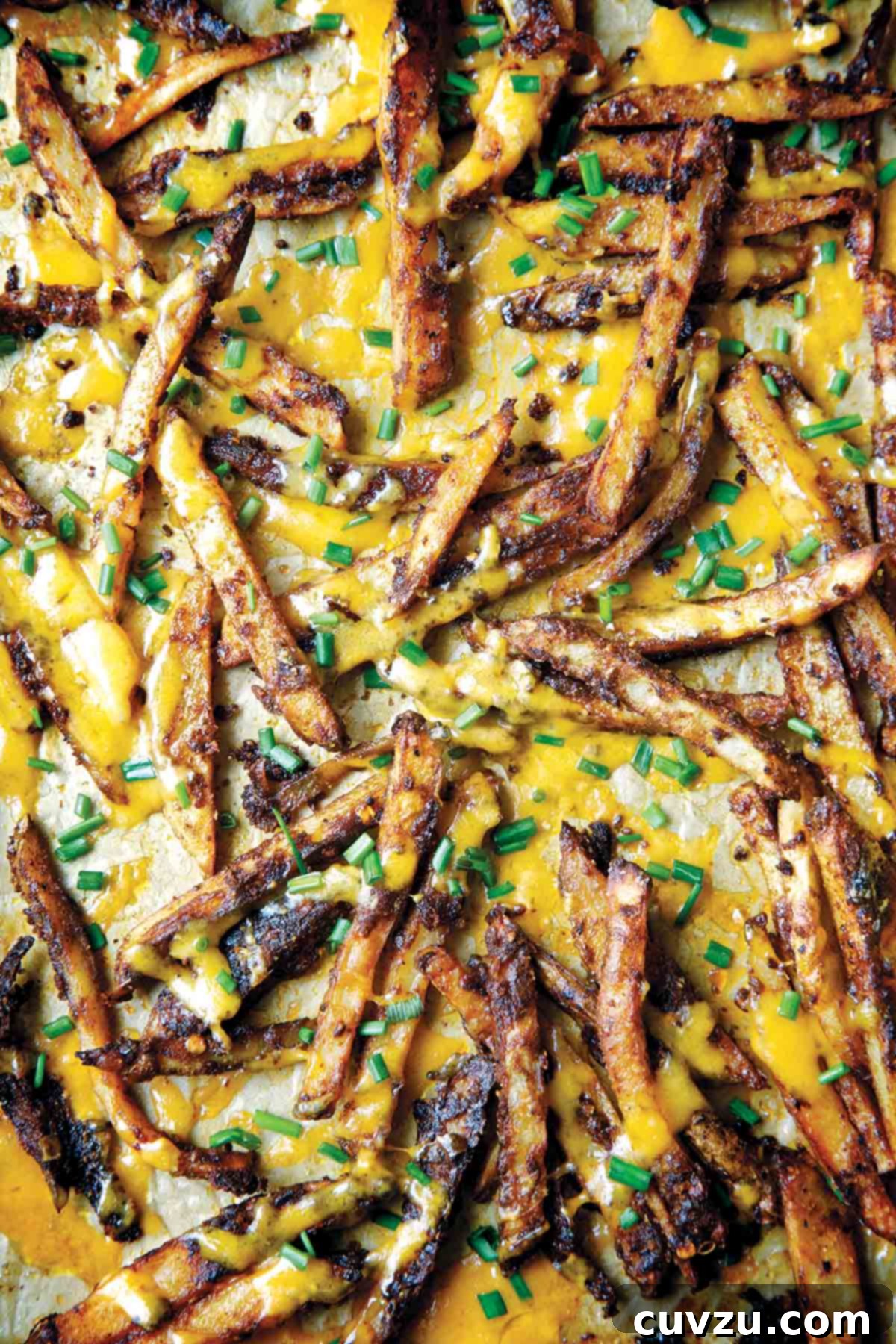 A scattering of chili cheese fries topped with melted cheddar and fresh snipped chives, served on a baking sheet.