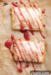 Two homemade toaster tarts on a sheet of parchment drizzled with glaze.