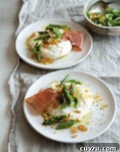 Two plates with burrata topped with asparagus, pine nuts, raisins, and prosciutto.