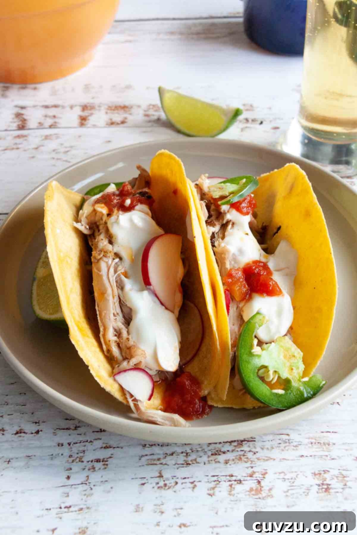 Carnitas: Authentic Mexican Braised Pork 8 Two pork tacos filled with shredded pork, radishes, jalapenos, salsa, and sour cream on a plate.