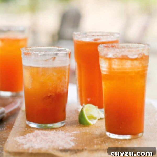 Four glasses of michelada on a wooden board with a lime wedge in between them.