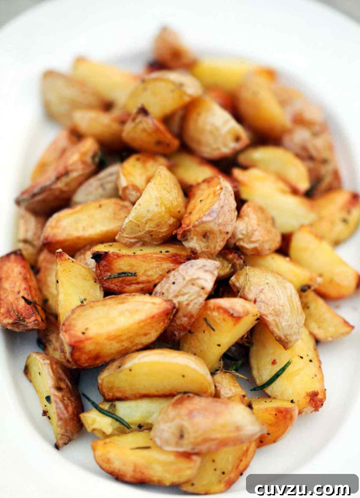 Smoky Golden Grilled Potatoes 7 A platter of quartered roasted potatoes on the grill, seasoned with pepper and rosemary.