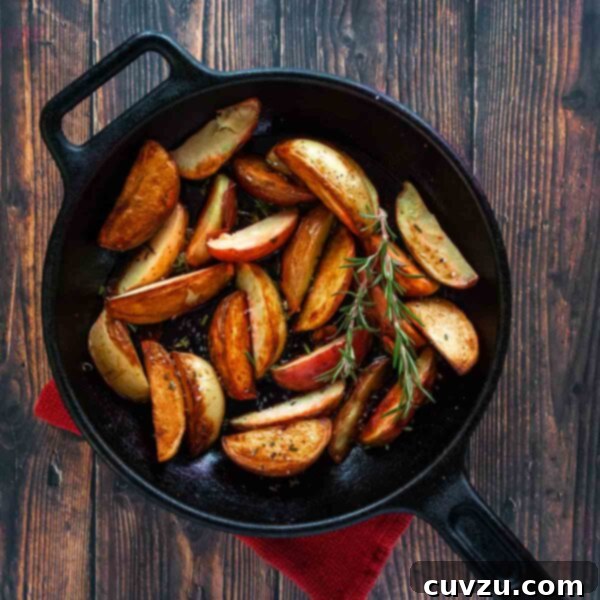 A cast-iron skillet filled with roasted grilled potatoes and two sprigs of rosemary on a wooden table.