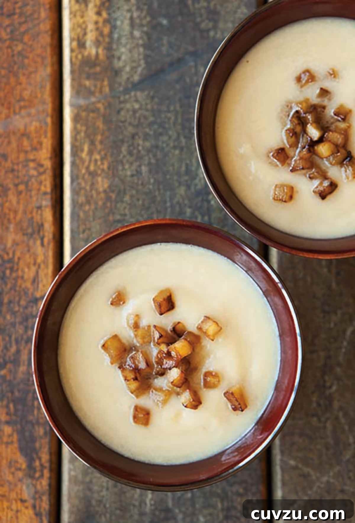 Golden Celeriac Velouté with Caramelized Apples 2 Two elegant bowls of smooth, pureed celery root soup, garnished generously with glistening cubes of caramelized apple, ready to be served.