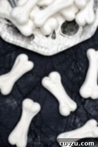 Halloween meringue bones piled on a paper plate and scattered on a black cobweb tablecloth beside the plate.