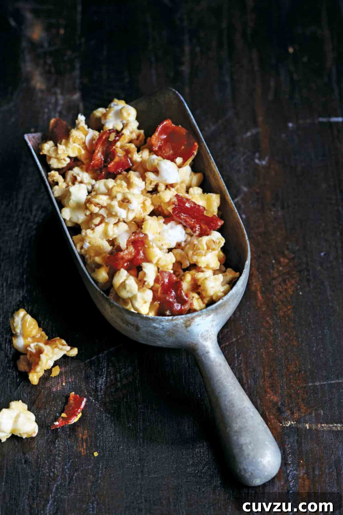 Smoky Sweet Bacon Reserve 5 A metal scoop filled to the brim with irresistible bacon bourbon butterscotch popcorn, ready for snacking.