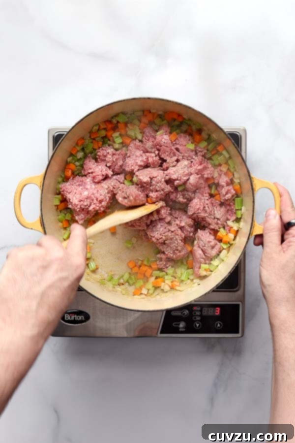 Marcella Hazan's Classic Bolognese 9 Ground beef, veal, and pork browning in a Dutch oven, being stirred with a wooden spoon.