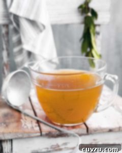 A large measuring cup of slow cooker chicken stock on a wooden table with a ladle on the side.